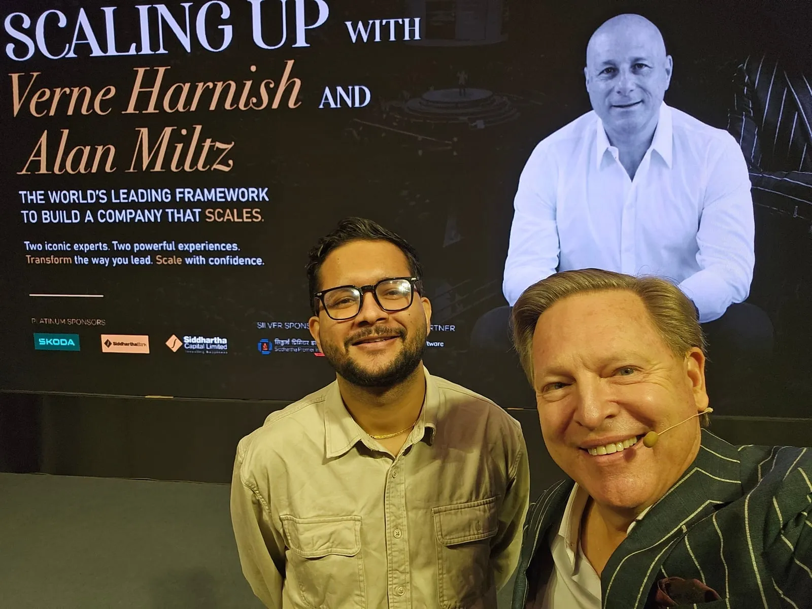 Bimal Raj Paudel with Verne Harnish at the Scaling Up with Verne Harnish and Alan Miltz event in Kathmandu, with Alan Miltz appearing on the screen behind them.